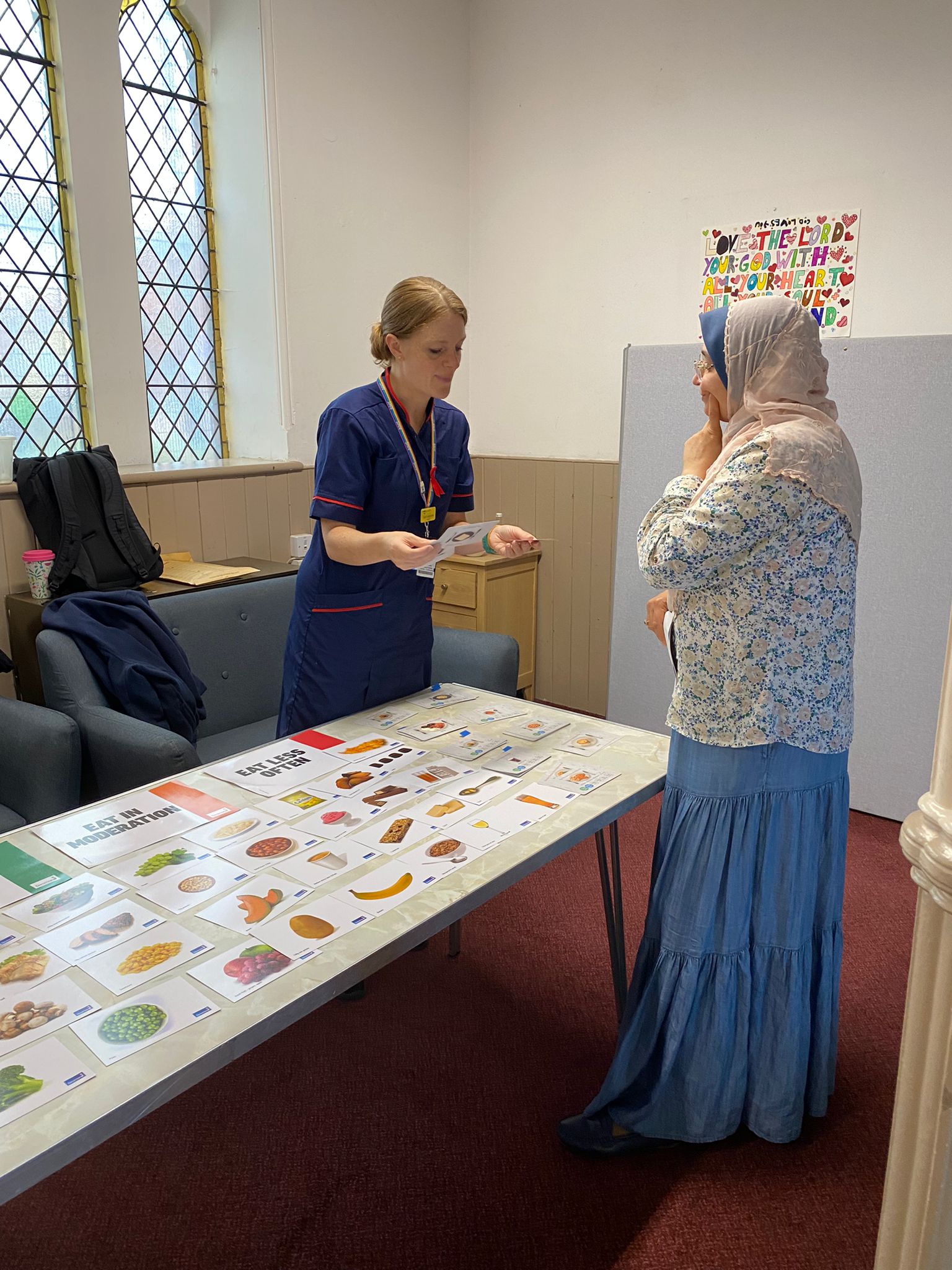 A health professional at a stall shows some information to an interested looking woman wearing a headscarf
