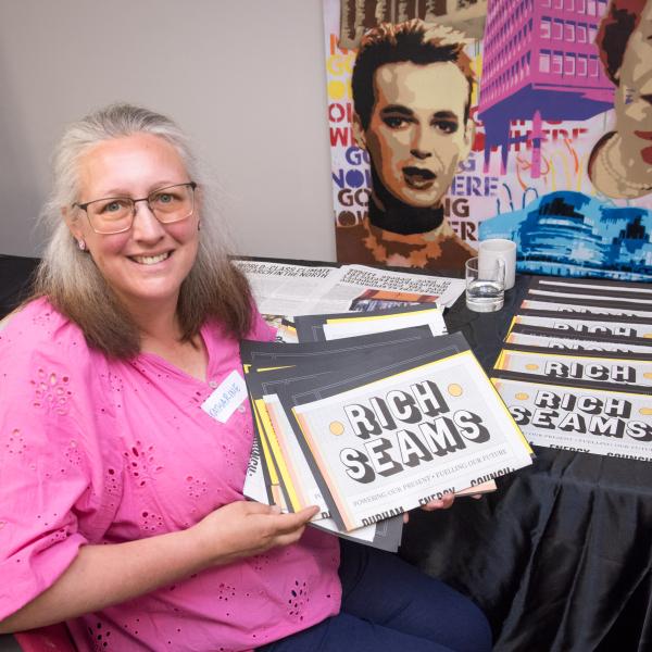 Woman holding up newspapers with Title 'Rich Seams'